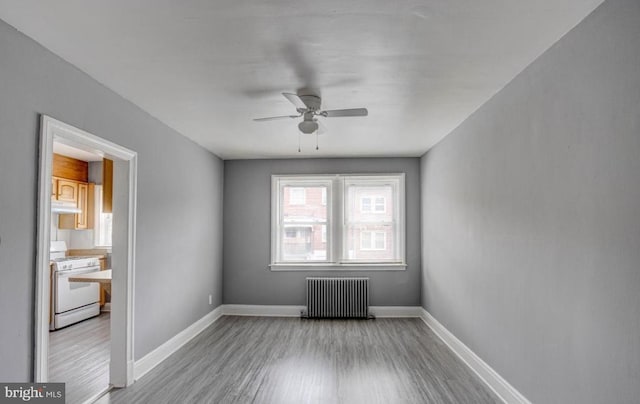 empty room with ceiling fan, light wood-type flooring, and radiator