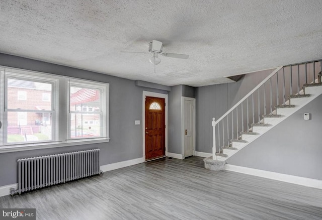 foyer with ceiling fan, light wood-type flooring, radiator heating unit, and a textured ceiling