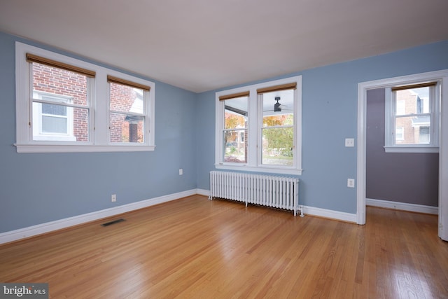 empty room with light hardwood / wood-style floors, radiator, a healthy amount of sunlight, and ceiling fan