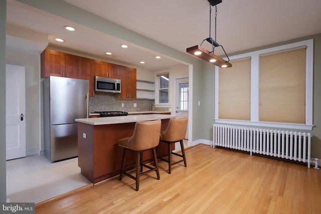 kitchen featuring decorative backsplash, light wood-type flooring, decorative light fixtures, radiator heating unit, and stainless steel appliances