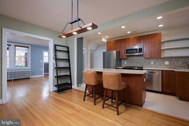 kitchen with a center island, radiator, light wood-type flooring, decorative light fixtures, and stainless steel appliances