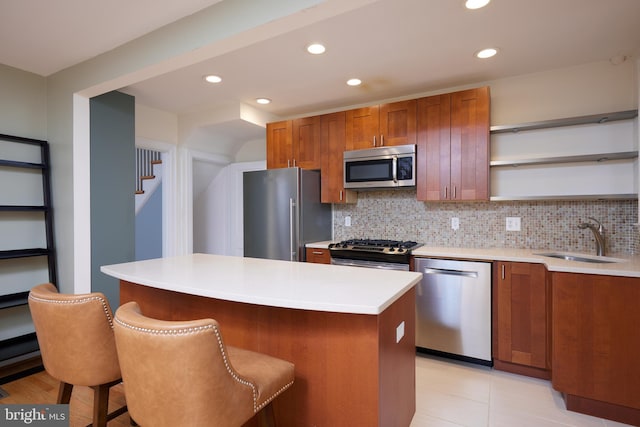 kitchen featuring sink, decorative backsplash, appliances with stainless steel finishes, a kitchen island, and a kitchen bar