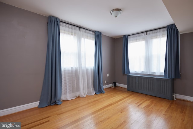 empty room with radiator, a healthy amount of sunlight, and wood-type flooring