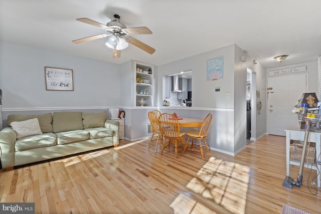 living room with ceiling fan, light hardwood / wood-style floors, built in features, and sink