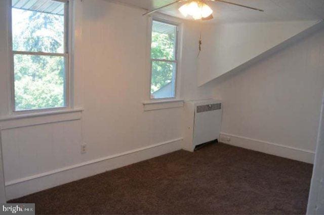 carpeted empty room with radiator, a healthy amount of sunlight, and ceiling fan