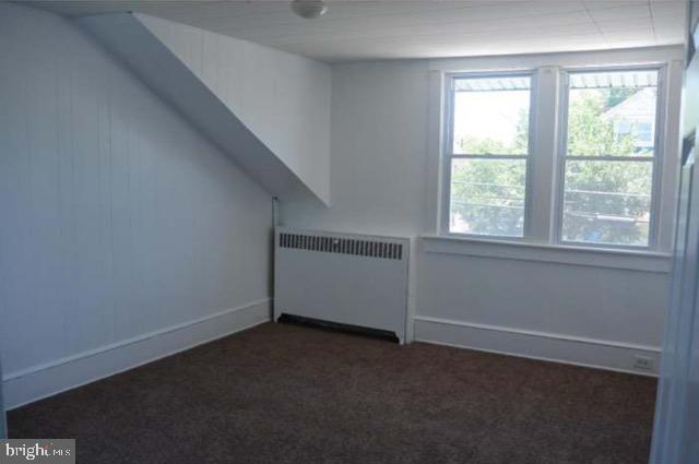 additional living space with dark colored carpet and radiator heating unit