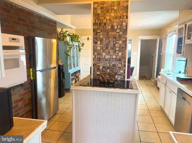 kitchen featuring white cabinetry, light tile patterned flooring, brick wall, and appliances with stainless steel finishes