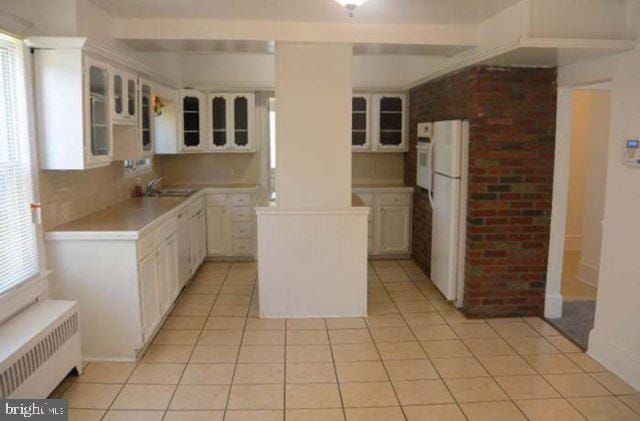 kitchen with backsplash, light tile patterned floors, radiator heating unit, white fridge, and white cabinetry