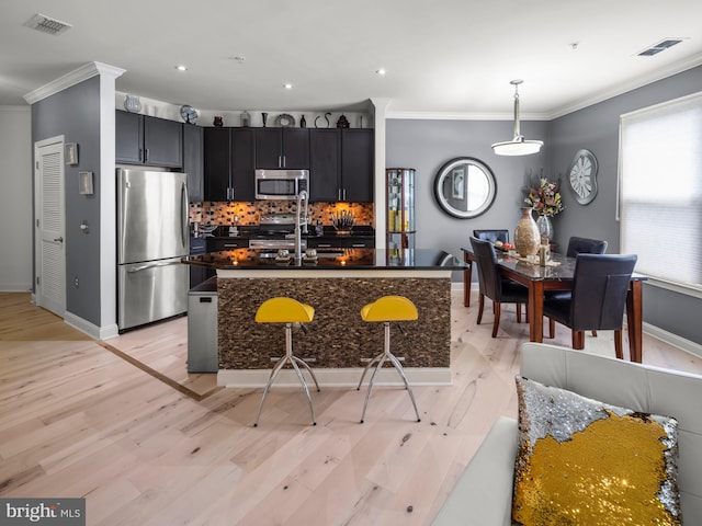 kitchen featuring backsplash, crown molding, light wood-type flooring, decorative light fixtures, and stainless steel appliances