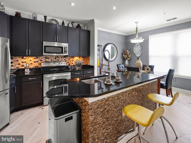 kitchen with a breakfast bar, stainless steel appliances, decorative light fixtures, light hardwood / wood-style flooring, and a center island with sink