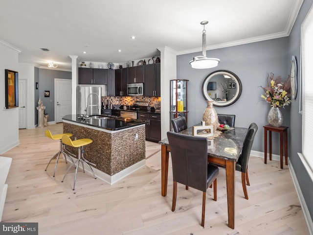 kitchen with sink, a kitchen island with sink, light hardwood / wood-style floors, decorative backsplash, and appliances with stainless steel finishes