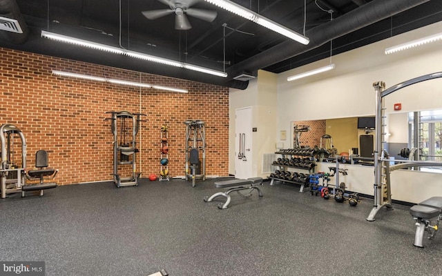 gym featuring a towering ceiling, ceiling fan, and brick wall