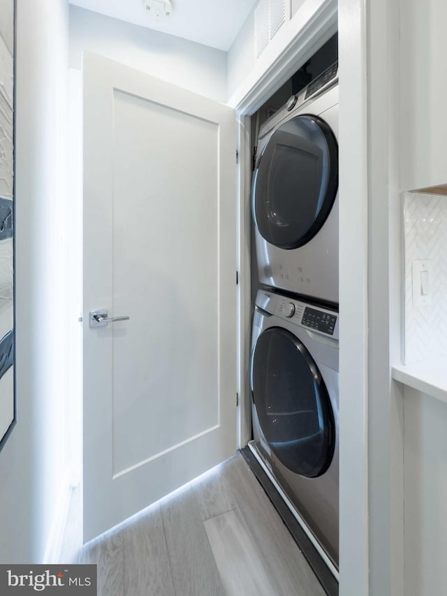 laundry room featuring stacked washer and clothes dryer and light hardwood / wood-style floors