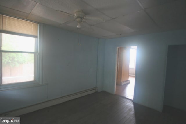 empty room with baseboard heating, a drop ceiling, dark wood-type flooring, and ceiling fan