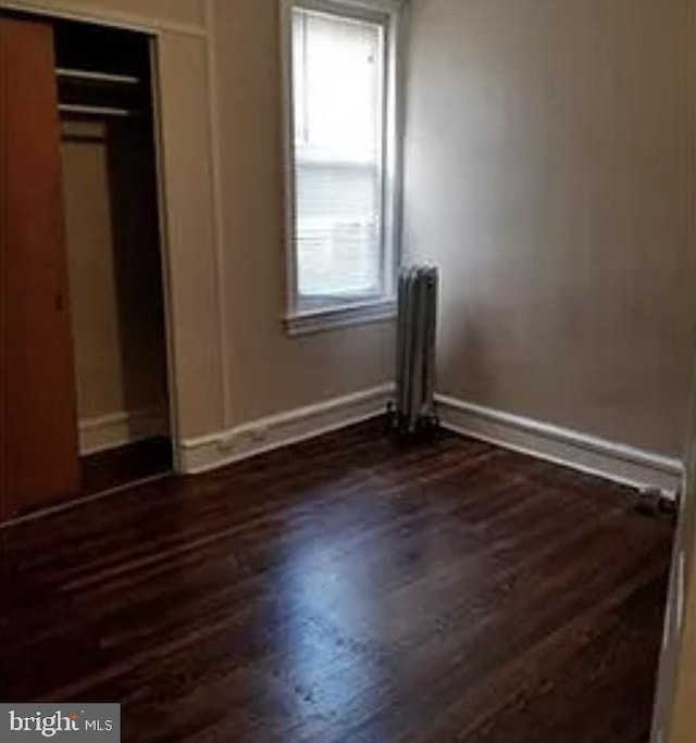 unfurnished bedroom featuring a closet, radiator heating unit, and dark hardwood / wood-style floors