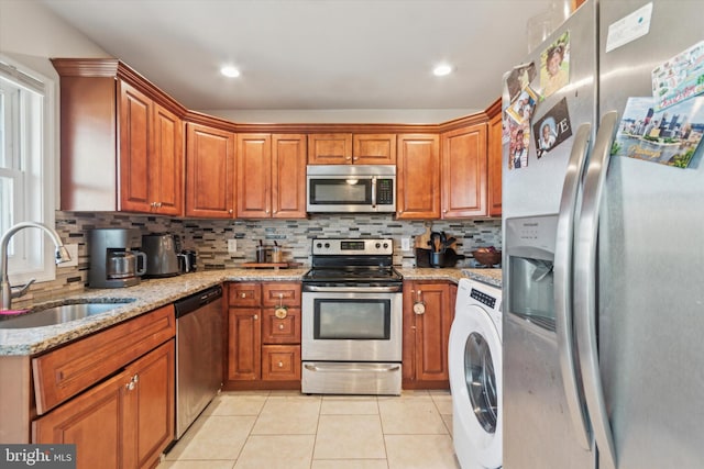 kitchen with light stone countertops, appliances with stainless steel finishes, sink, washer / dryer, and light tile patterned flooring