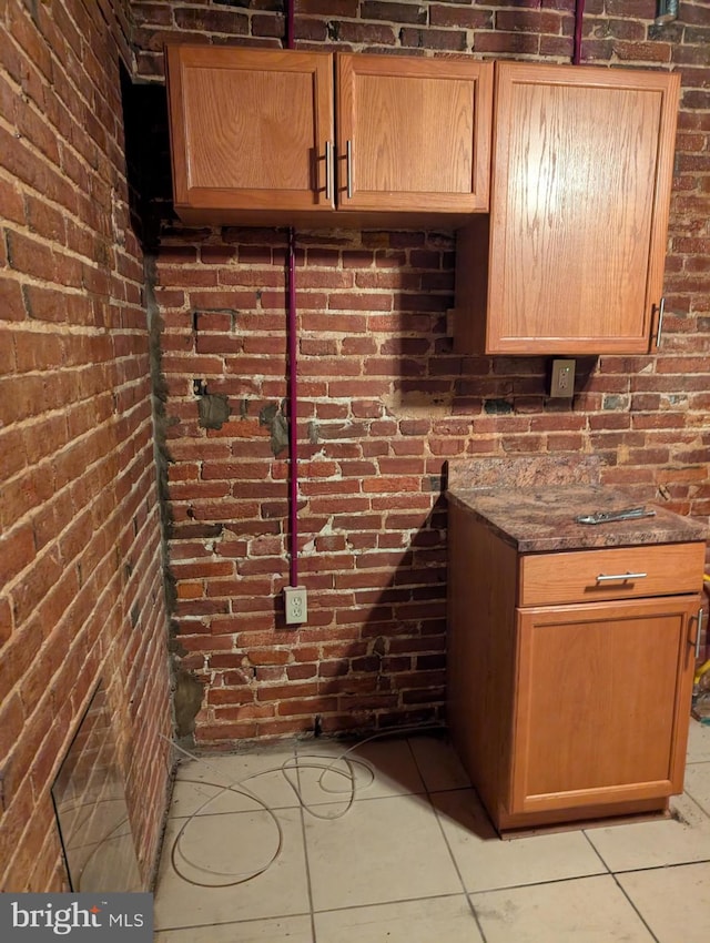 bar featuring light tile patterned floors, dark stone counters, and brick wall