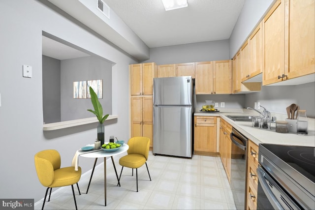 kitchen featuring light brown cabinets, a textured ceiling, stainless steel appliances, and sink