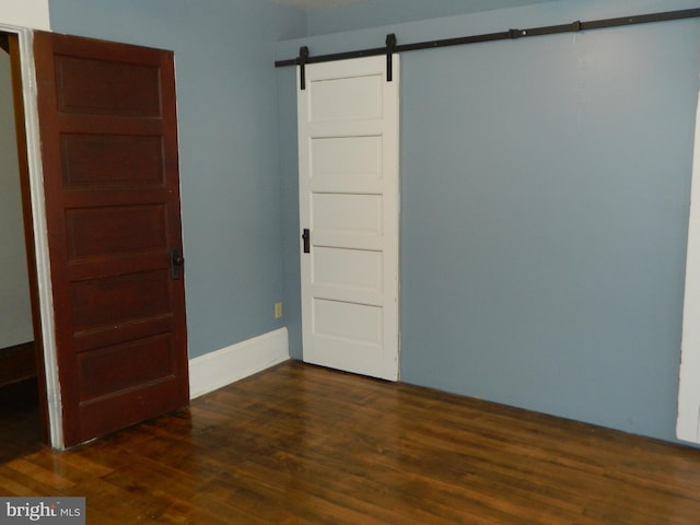 empty room with a barn door and dark wood-type flooring