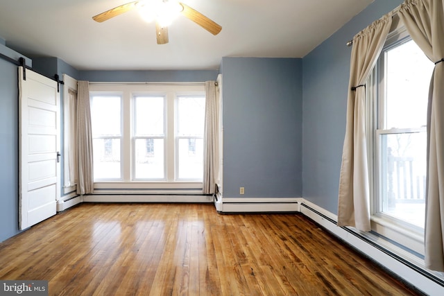 unfurnished room featuring ceiling fan, a barn door, wood-type flooring, and a baseboard heating unit