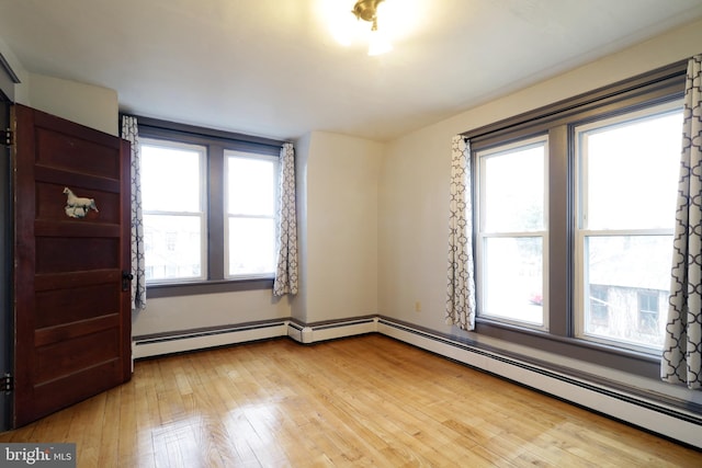 unfurnished room featuring light hardwood / wood-style floors, a wealth of natural light, and a baseboard heating unit