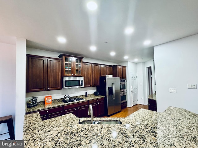 kitchen featuring appliances with stainless steel finishes, light hardwood / wood-style flooring, light stone counters, and sink