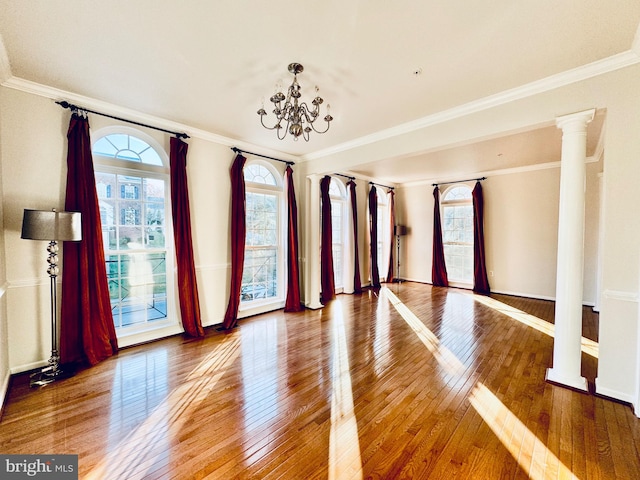 empty room with decorative columns, crown molding, hardwood / wood-style floors, and a chandelier