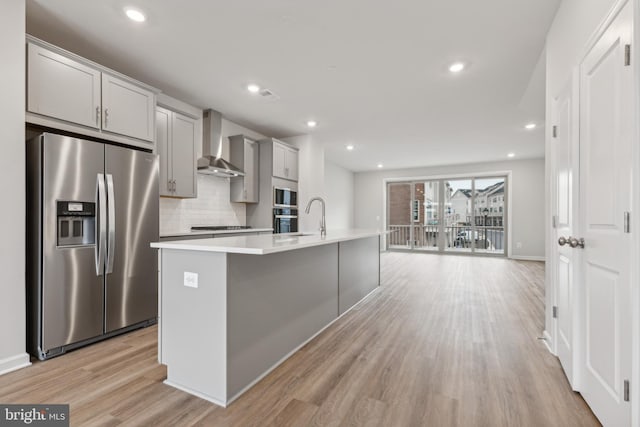 kitchen featuring a center island with sink, wall chimney exhaust hood, gray cabinets, light hardwood / wood-style floors, and stainless steel appliances