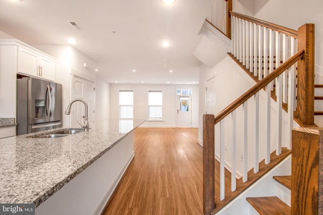 kitchen featuring sink, stainless steel fridge with ice dispenser, light stone countertops, light wood-type flooring, and white cabinetry