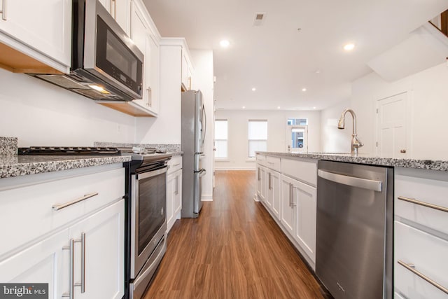 kitchen with light stone countertops, sink, wood-type flooring, white cabinets, and appliances with stainless steel finishes