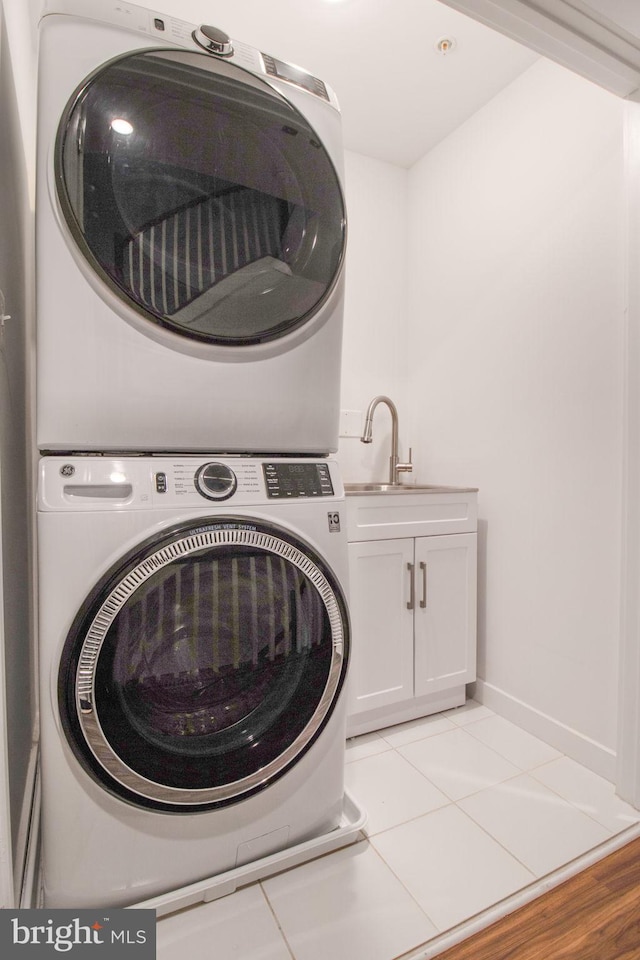 clothes washing area featuring sink, light tile patterned flooring, cabinets, and stacked washer and clothes dryer