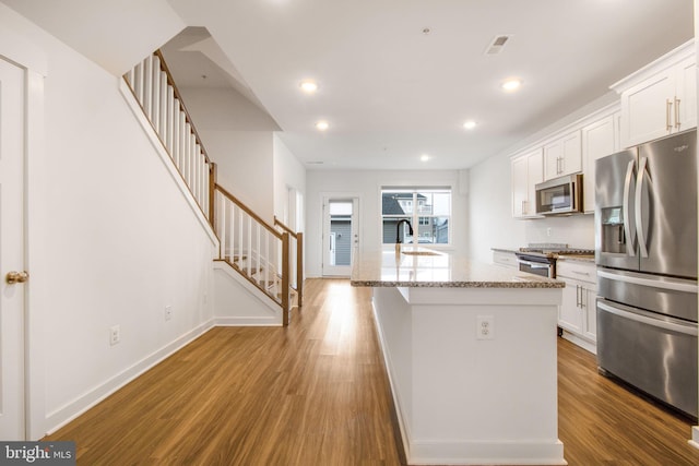 kitchen with an island with sink, hardwood / wood-style floors, white cabinets, and stainless steel appliances