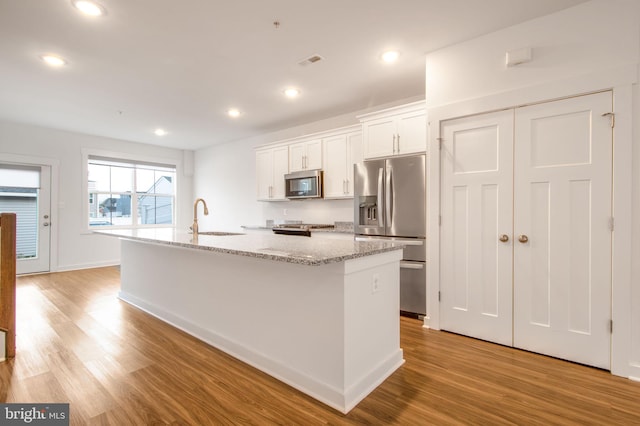 kitchen with a kitchen island with sink, white cabinets, sink, appliances with stainless steel finishes, and light hardwood / wood-style floors