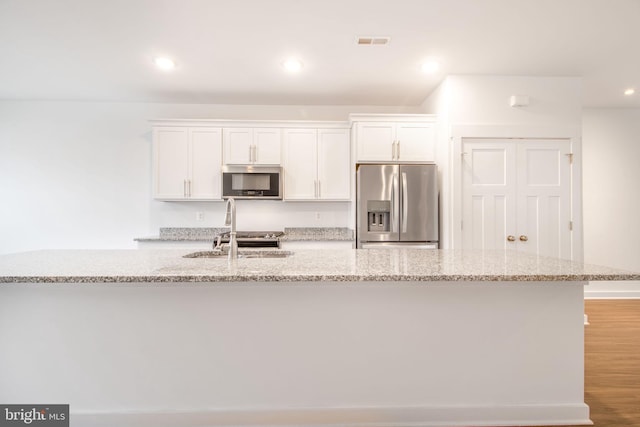 kitchen with light stone counters, white cabinetry, stainless steel appliances, and light hardwood / wood-style flooring