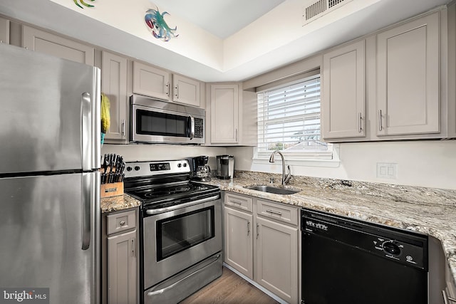 kitchen featuring appliances with stainless steel finishes, light stone counters, gray cabinetry, sink, and hardwood / wood-style floors