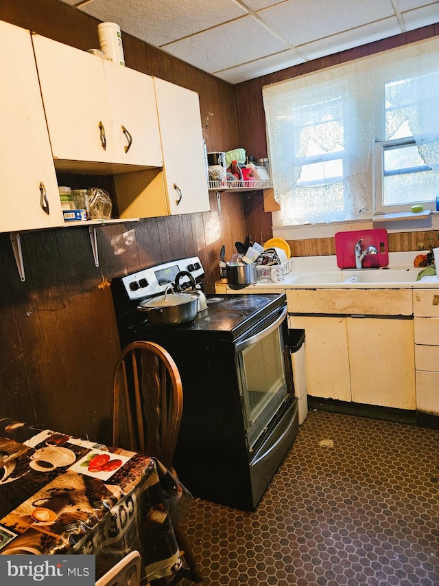 kitchen featuring white cabinetry, a paneled ceiling, wood walls, and black electric range