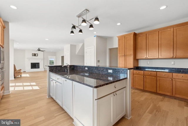 kitchen featuring a fireplace, a center island with sink, light wood-type flooring, and open floor plan
