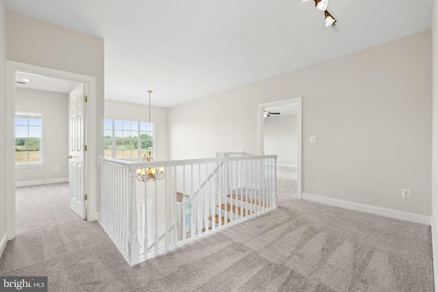 hall featuring an inviting chandelier, baseboards, carpet flooring, and an upstairs landing