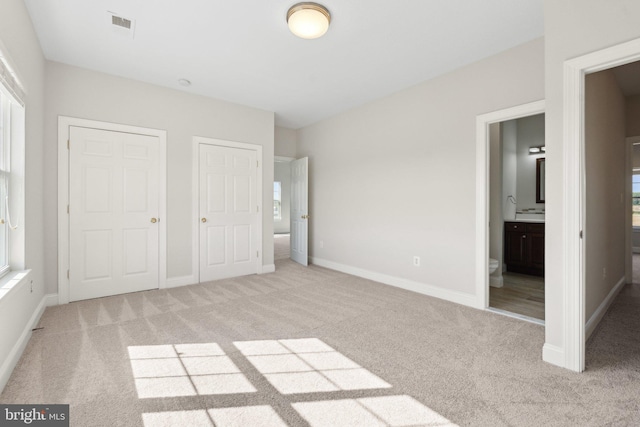 unfurnished bedroom featuring light colored carpet, baseboards, and ensuite bathroom