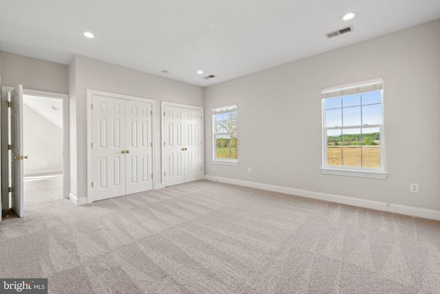 unfurnished bedroom with visible vents, carpet flooring, baseboards, and two closets