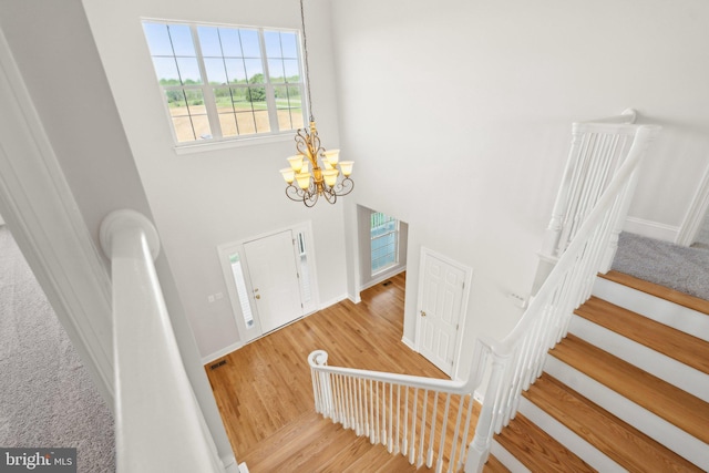 foyer entrance featuring an inviting chandelier, wood finished floors, baseboards, a high ceiling, and stairway