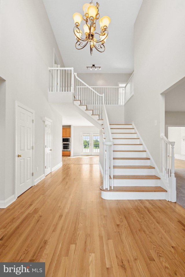 foyer entrance with a high ceiling, an inviting chandelier, stairs, baseboards, and light wood-type flooring