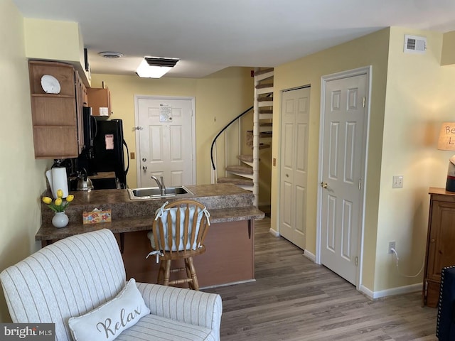 kitchen featuring kitchen peninsula, black fridge, sink, dark hardwood / wood-style floors, and a breakfast bar area