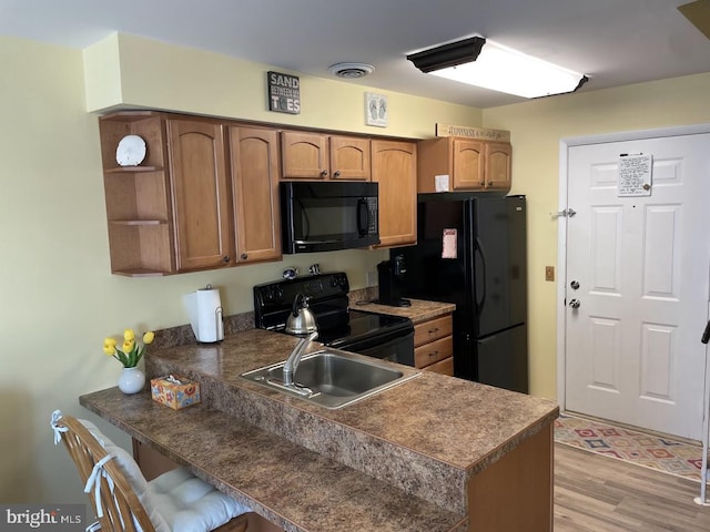 kitchen featuring kitchen peninsula, light hardwood / wood-style flooring, black appliances, and sink