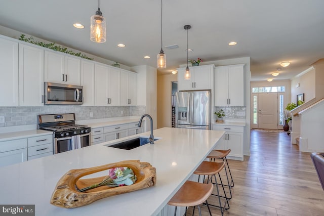 kitchen featuring hanging light fixtures, sink, light hardwood / wood-style flooring, appliances with stainless steel finishes, and white cabinetry