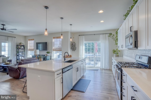 kitchen with white cabinetry, sink, light hardwood / wood-style floors, a kitchen island with sink, and appliances with stainless steel finishes