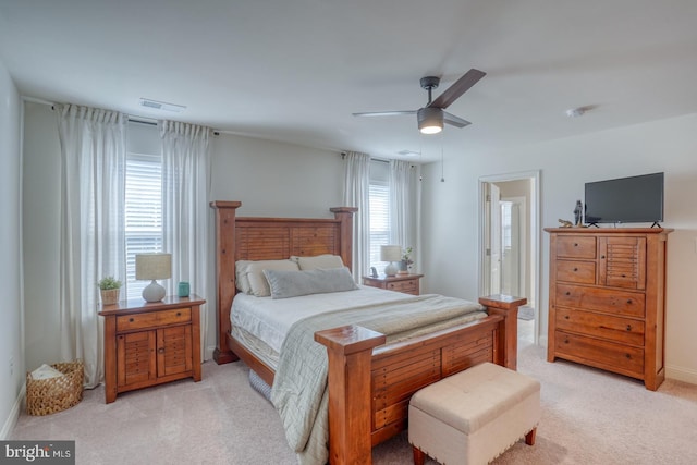 bedroom with ceiling fan, light colored carpet, and ensuite bath