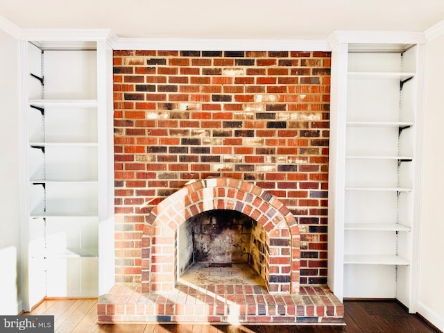 room details with hardwood / wood-style flooring, built in shelves, crown molding, and a brick fireplace