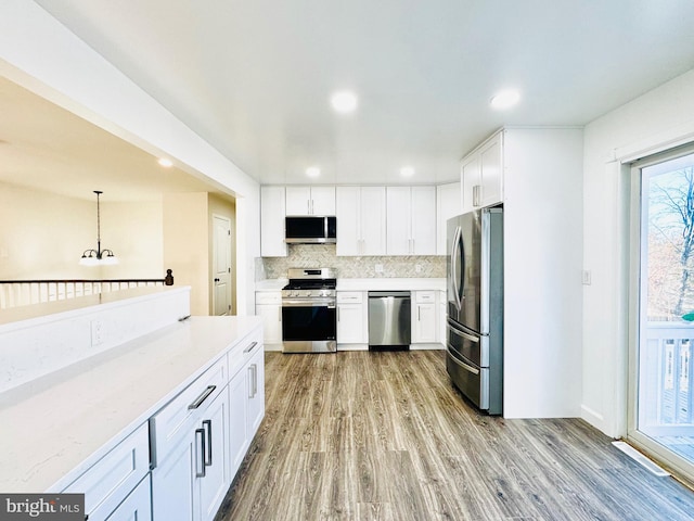 kitchen with white cabinets, pendant lighting, backsplash, and stainless steel appliances