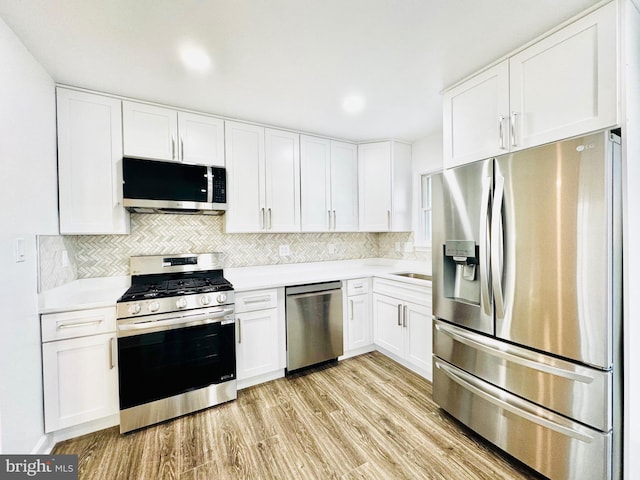 kitchen with appliances with stainless steel finishes, tasteful backsplash, sink, light hardwood / wood-style flooring, and white cabinets